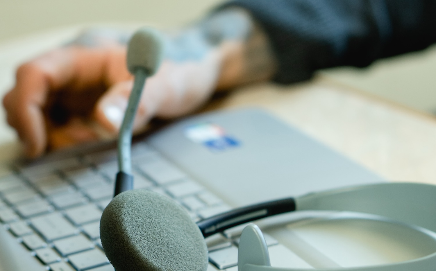 Hand on a laptop and a headset.